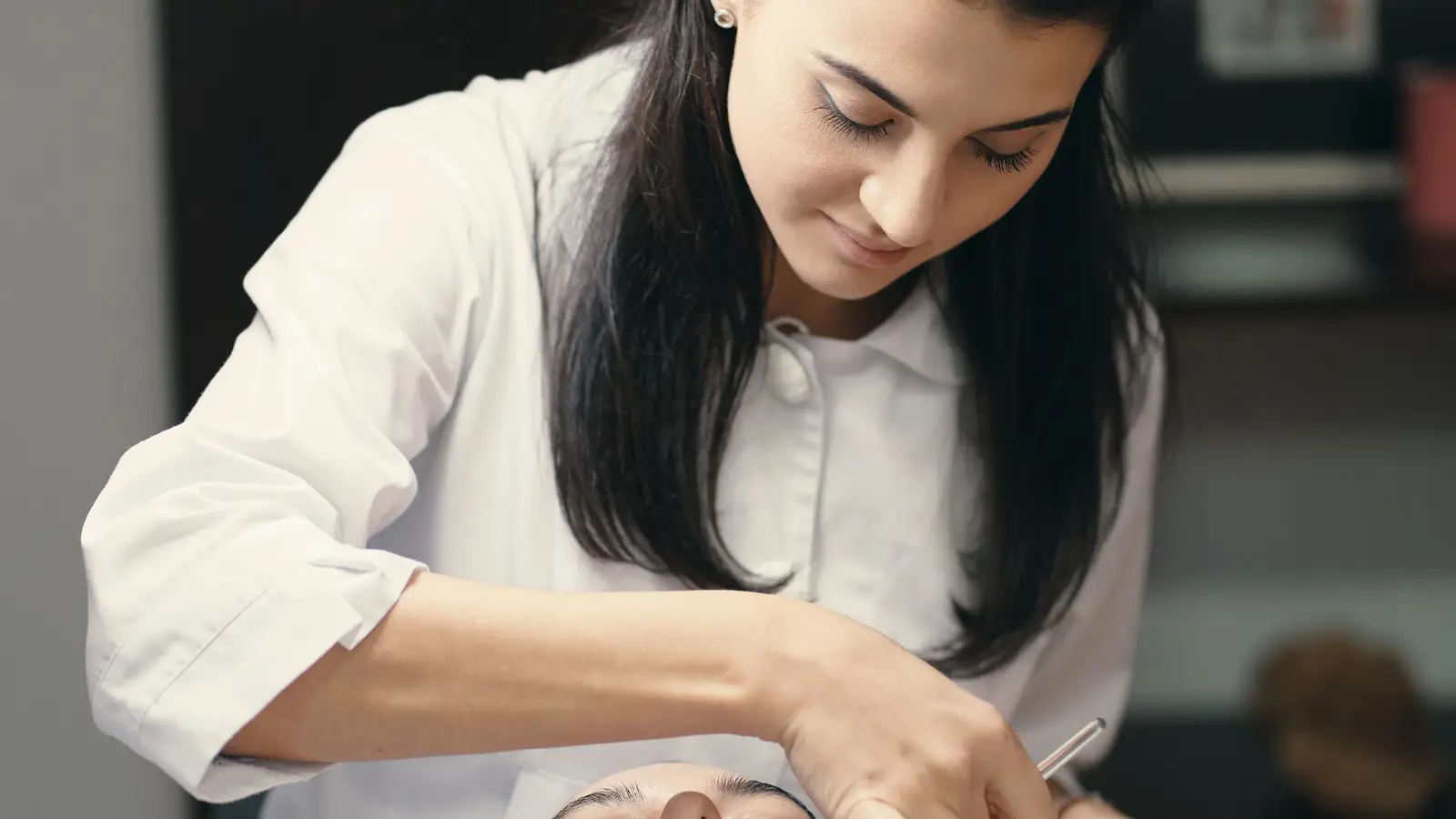 An esthetician in a white coat leaning over a client during a facial treatment