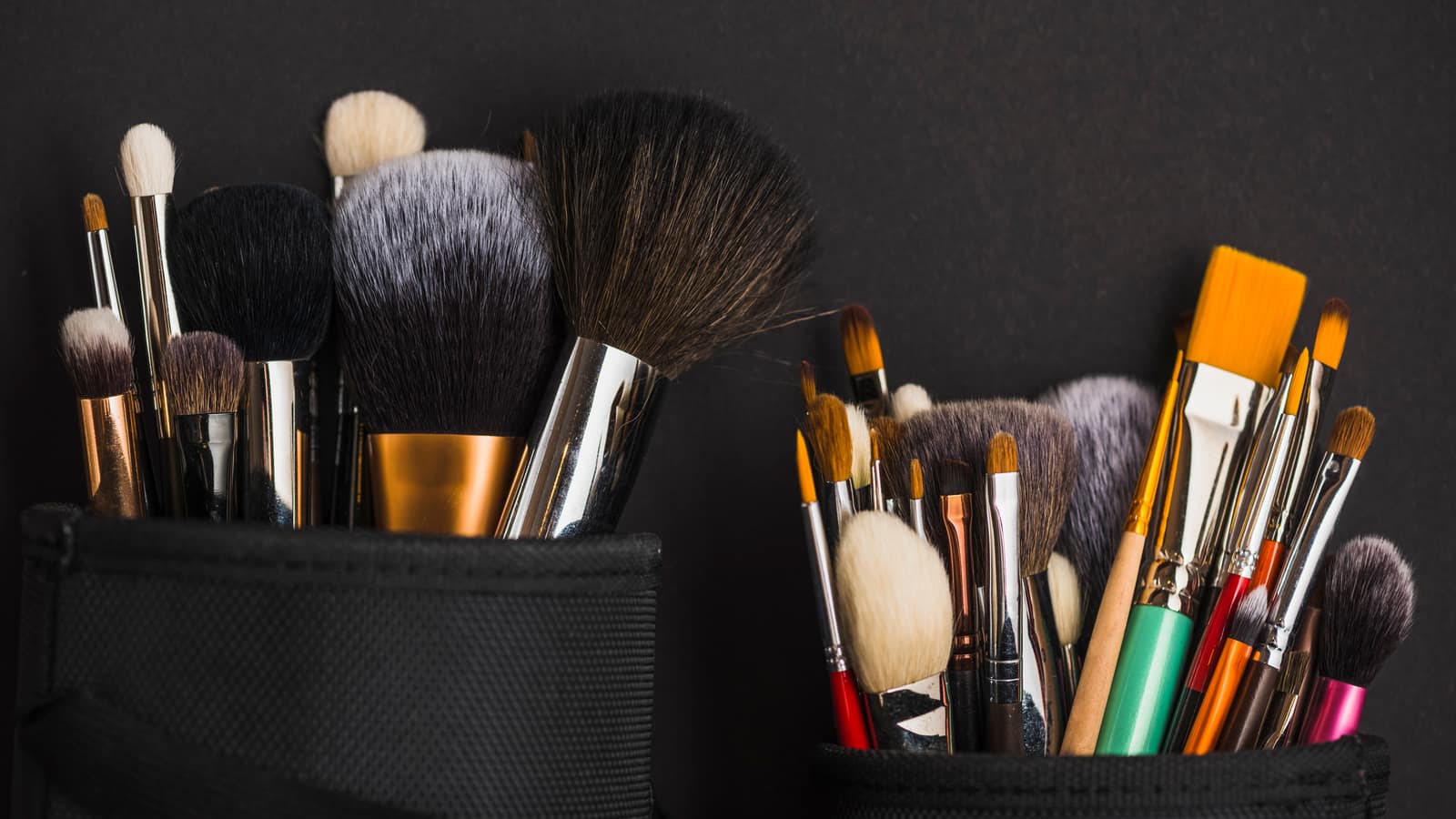 Two rolls of makeup brushes of many shapes standing open against a dark background