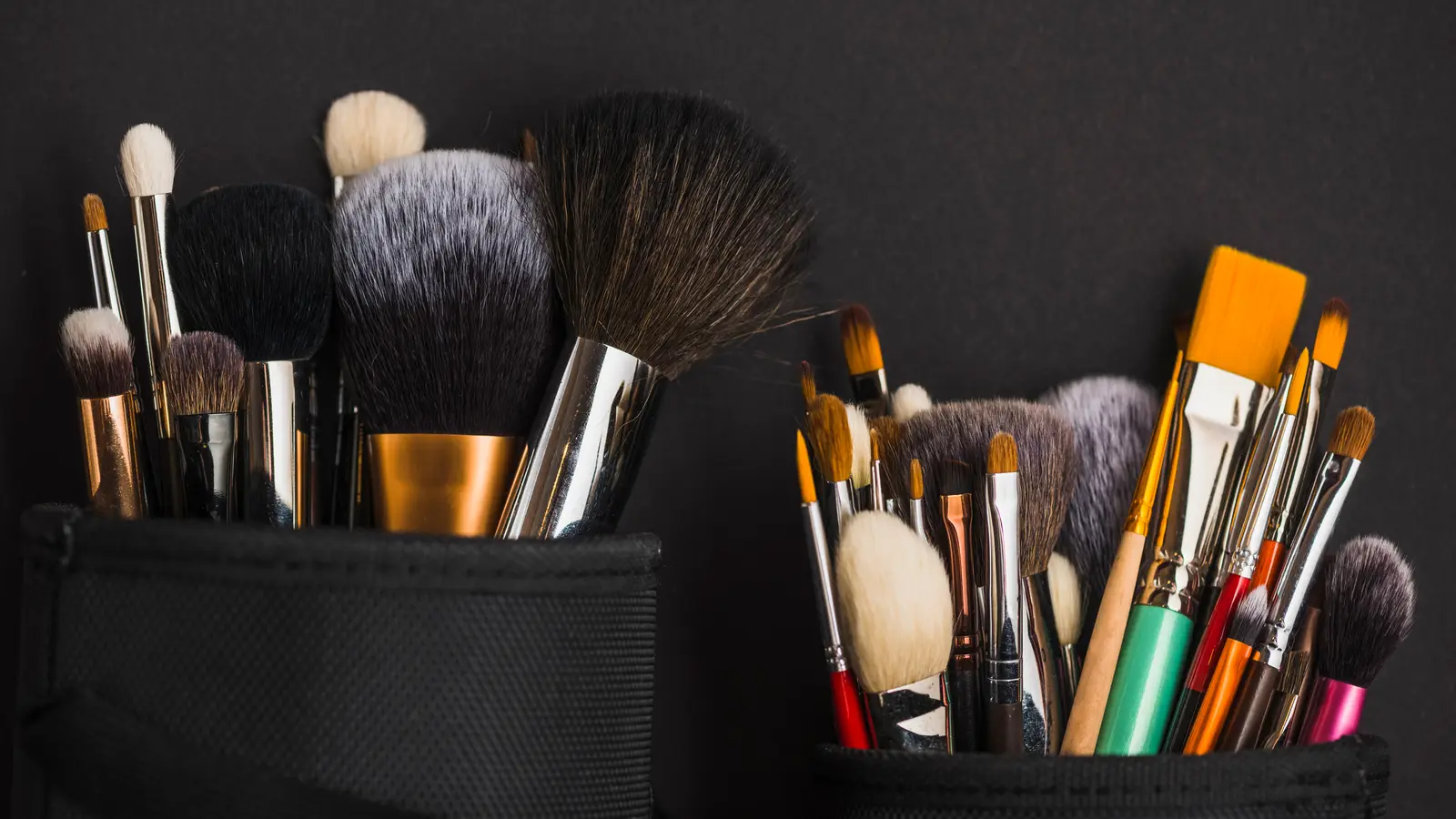 Two rolls of makeup brushes of many shapes standing open against a dark background